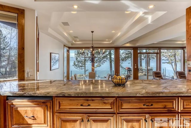 kitchen featuring a raised ceiling, hanging light fixtures, a notable chandelier, and light stone countertops