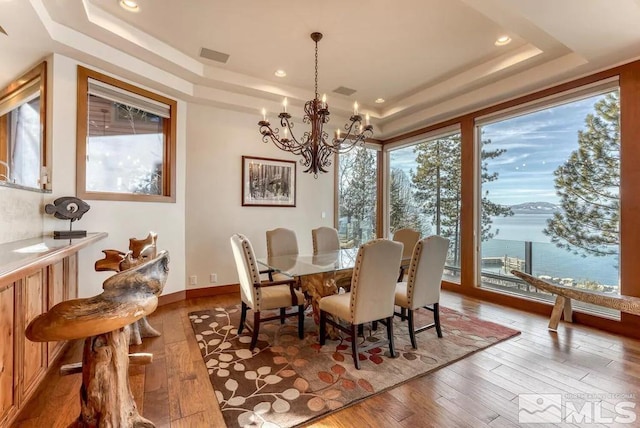 dining room with an inviting chandelier, a tray ceiling, hardwood / wood-style flooring, and a water view