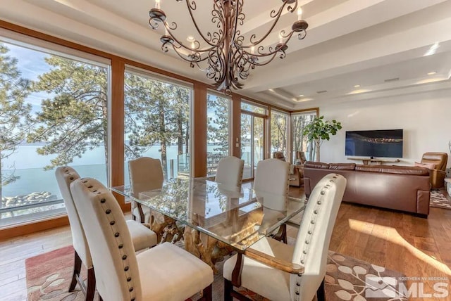 dining area featuring a notable chandelier, light wood-type flooring, and a raised ceiling