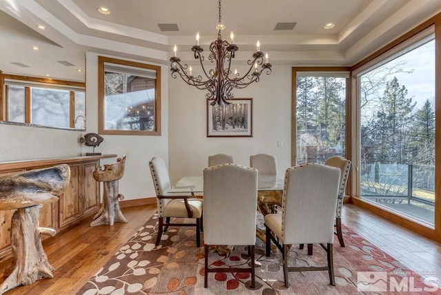 dining space with a notable chandelier, a tray ceiling, and light wood-type flooring