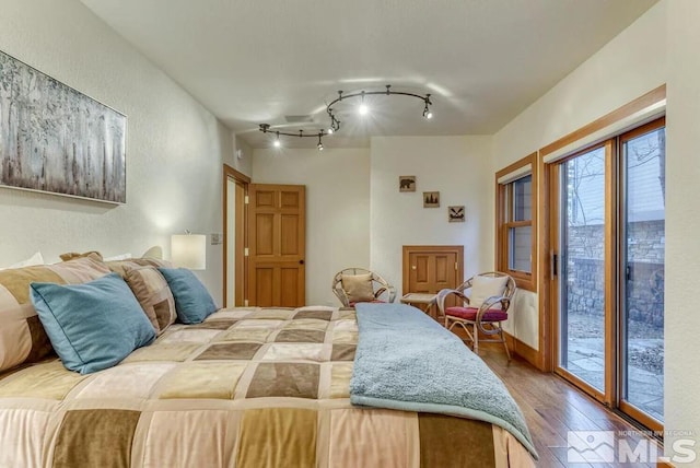 bedroom with rail lighting, access to outside, and hardwood / wood-style flooring