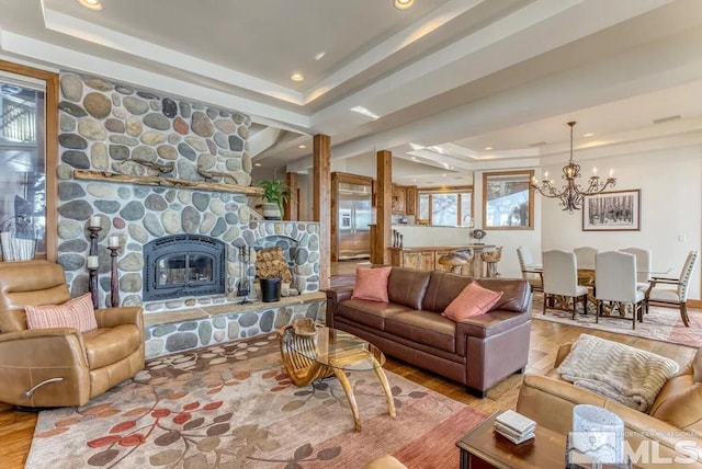 living room featuring a wealth of natural light, a chandelier, light hardwood / wood-style floors, a stone fireplace, and a raised ceiling