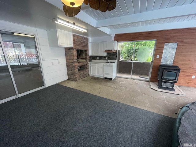 interior space with ceiling fan, a wood stove, beamed ceiling, and white cabinets