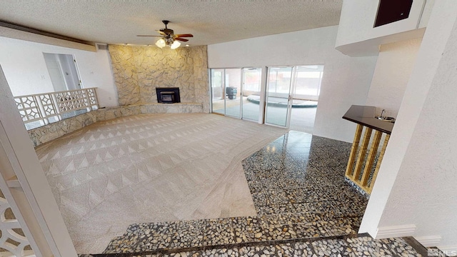 living room with ceiling fan, a stone fireplace, and a textured ceiling