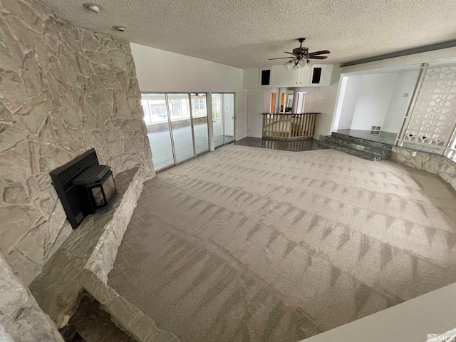 unfurnished living room featuring a fireplace, ceiling fan, a wood stove, and light colored carpet