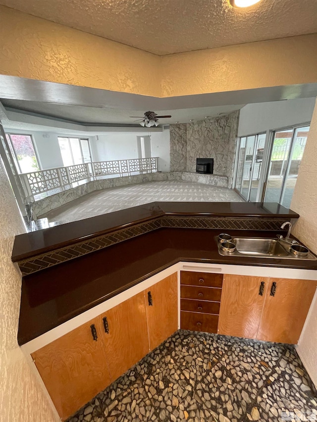 kitchen featuring ceiling fan, sink, a fireplace, and a textured ceiling