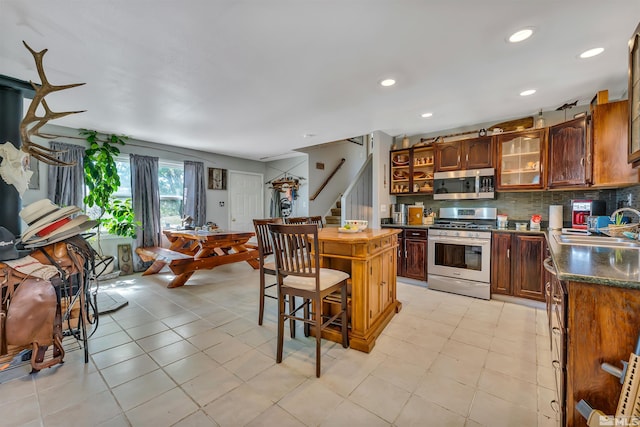 kitchen featuring backsplash, range with gas cooktop, sink, and light tile floors