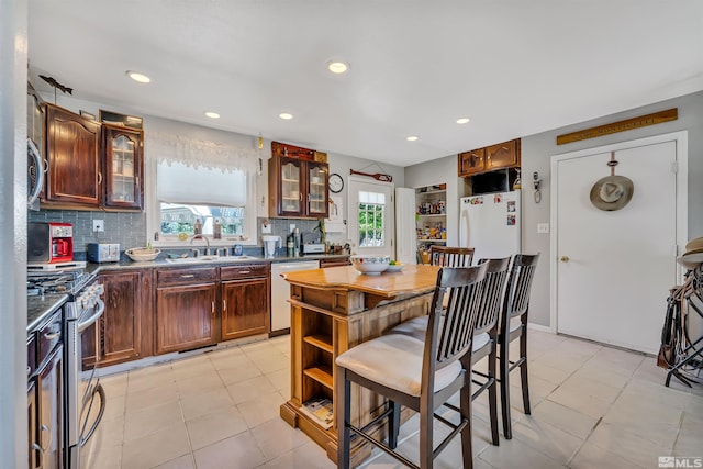 kitchen with a kitchen bar, tasteful backsplash, white appliances, and light tile floors