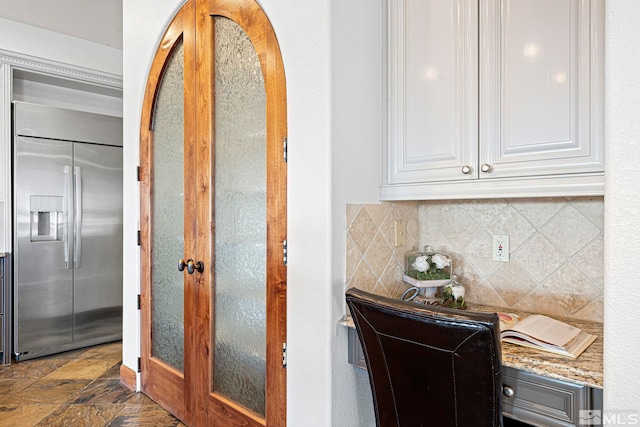 interior space with backsplash, dark tile floors, white cabinets, stainless steel built in fridge, and light stone counters