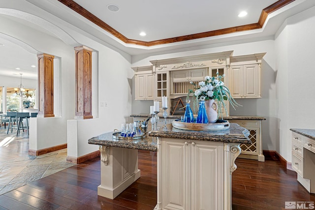 kitchen with dark stone counters, a kitchen island, a chandelier, and decorative columns