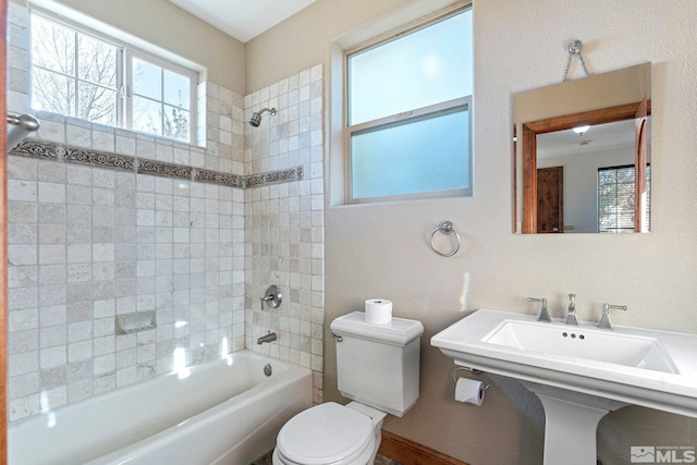 bathroom with tiled shower / bath combo, toilet, and a healthy amount of sunlight