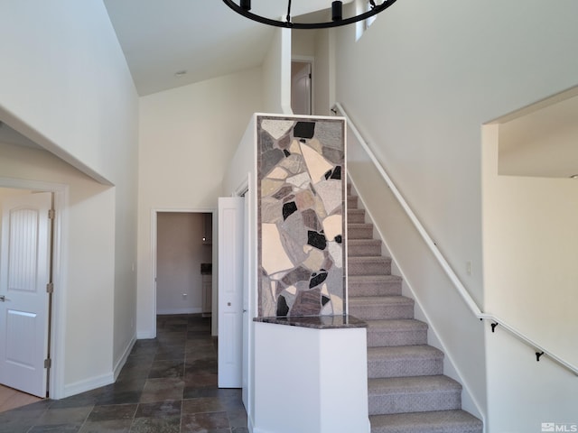 staircase with dark tile floors, a high ceiling, and an inviting chandelier