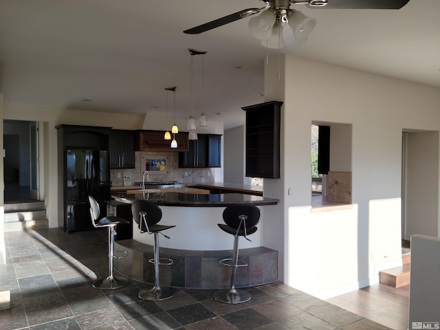 kitchen featuring tasteful backsplash, ceiling fan, decorative light fixtures, a kitchen breakfast bar, and black fridge