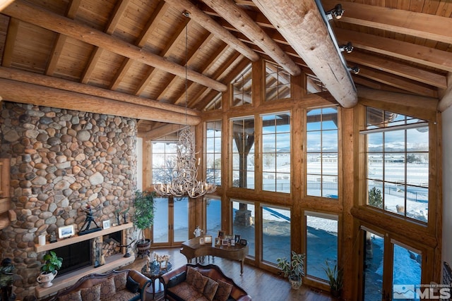 interior space featuring a notable chandelier, beam ceiling, wood ceiling, a stone fireplace, and dark hardwood / wood-style flooring