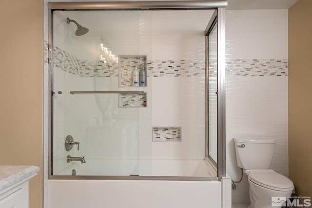 full bathroom with tile walls, toilet, vanity, and bath / shower combo with glass door