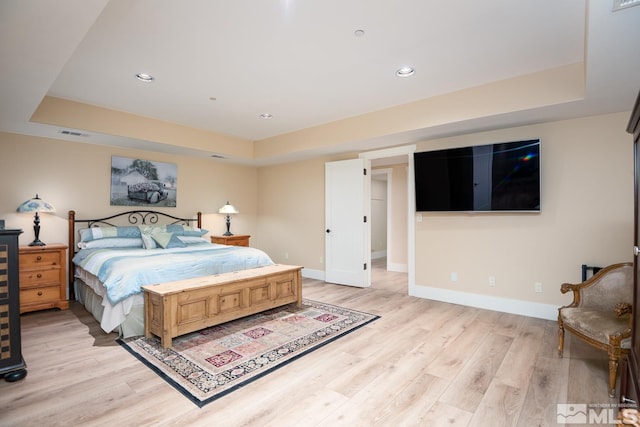 bedroom with a tray ceiling and light wood-type flooring