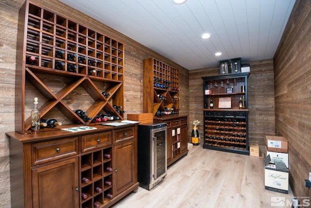 wine room featuring indoor bar, light hardwood / wood-style floors, wood walls, and beverage cooler