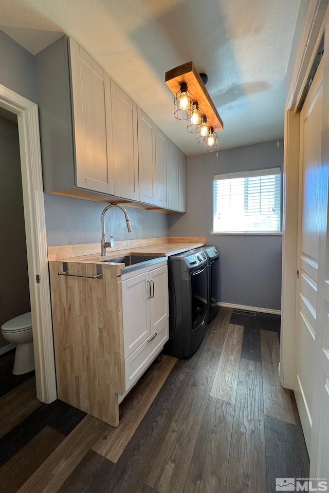 clothes washing area featuring dark hardwood / wood-style flooring, sink, cabinets, and washer and clothes dryer