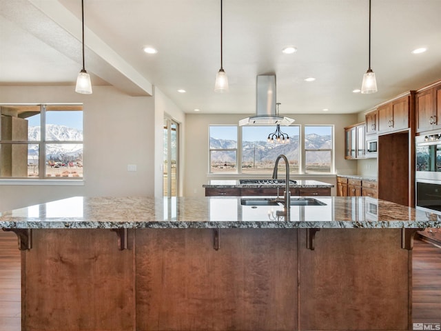 kitchen with decorative light fixtures, island range hood, a healthy amount of sunlight, and hardwood / wood-style flooring