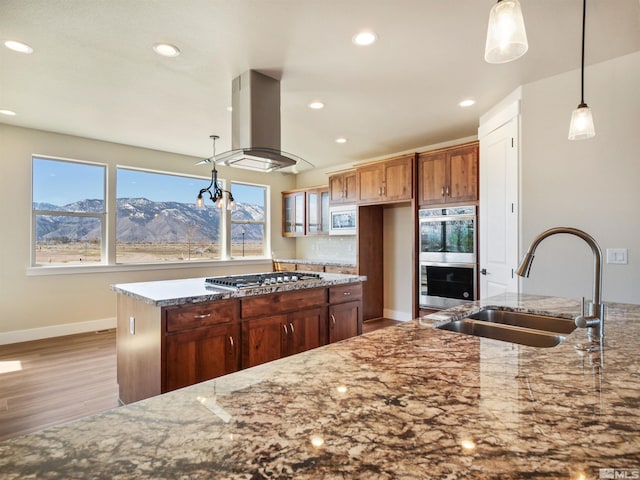 kitchen with appliances with stainless steel finishes, light stone counters, sink, island exhaust hood, and light hardwood / wood-style flooring