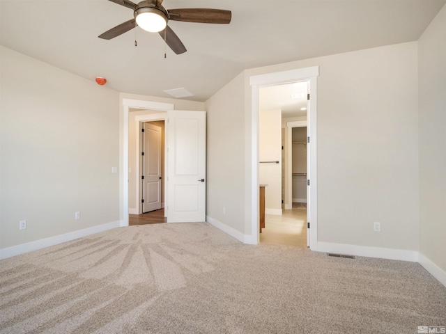 unfurnished bedroom featuring light carpet, a spacious closet, ceiling fan, and lofted ceiling