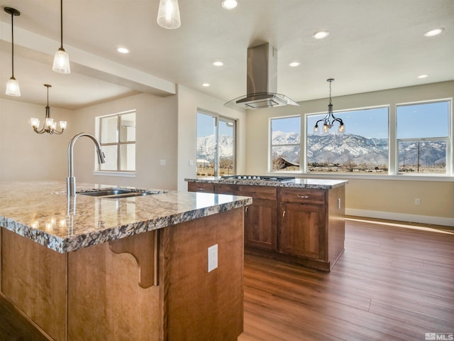 kitchen with hanging light fixtures, a mountain view, a center island with sink, island range hood, and dark hardwood / wood-style flooring