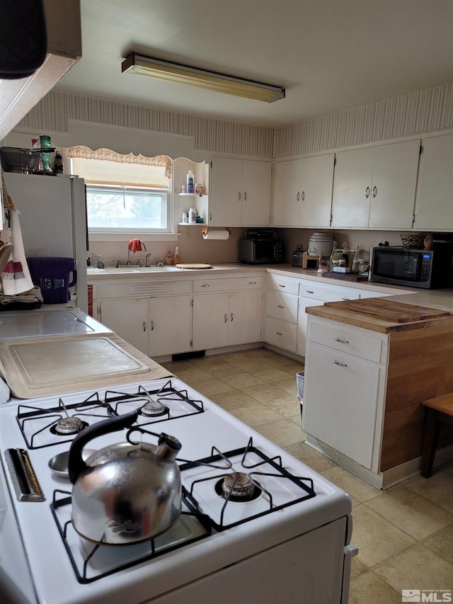 kitchen featuring white cabinetry, light tile flooring, sink, stove, and white refrigerator