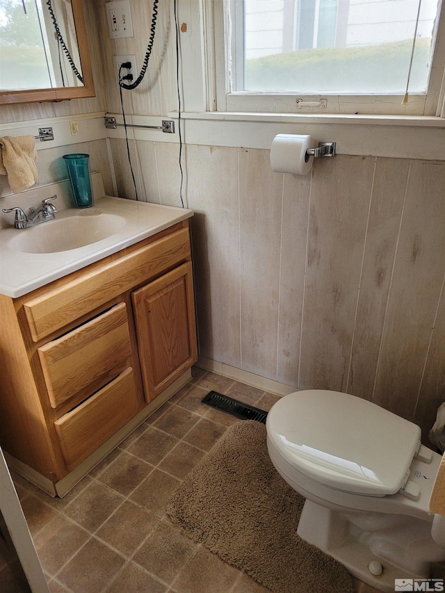 bathroom featuring toilet, wood walls, tile floors, and vanity