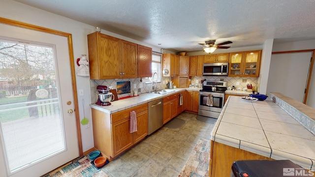 kitchen with stainless steel appliances, light tile floors, ceiling fan, tasteful backsplash, and tile counters