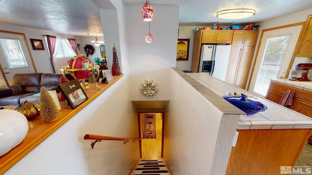 interior space with white refrigerator with ice dispenser, tile counters, decorative light fixtures, and a textured ceiling