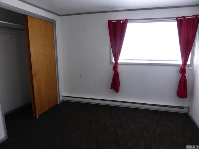 unfurnished bedroom featuring a closet, baseboard heating, and dark wood-type flooring