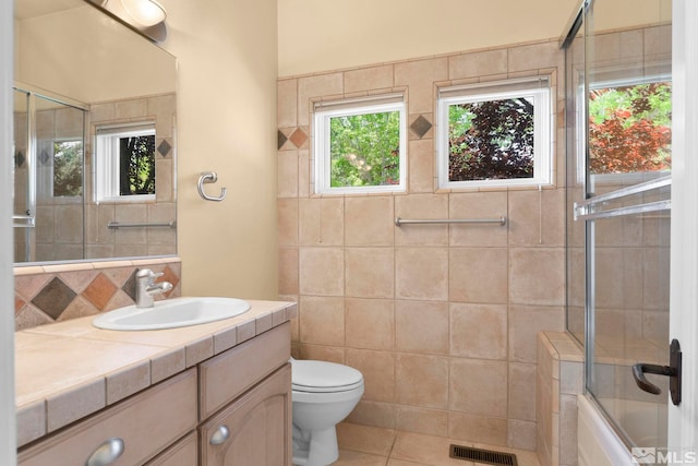 full bathroom with toilet, vanity with extensive cabinet space, tile walls, combined bath / shower with glass door, and tile flooring