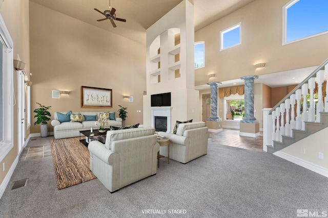 carpeted living room featuring ornate columns, ceiling fan, and a towering ceiling