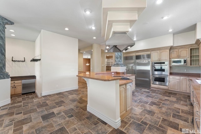 kitchen featuring dark tile floors, dark stone countertops, built in appliances, and a kitchen island with sink