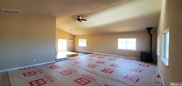 carpeted empty room with plenty of natural light, a wood stove, ceiling fan, and vaulted ceiling