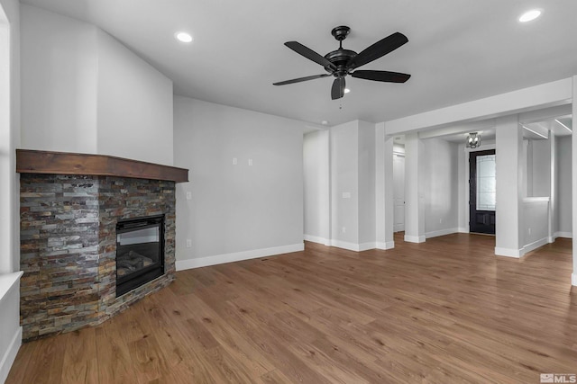 unfurnished living room featuring hardwood / wood-style floors, a stone fireplace, and ceiling fan