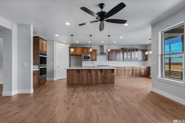 kitchen with wall chimney exhaust hood, light hardwood / wood-style floors, ceiling fan, and appliances with stainless steel finishes