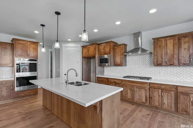 kitchen featuring appliances with stainless steel finishes, hanging light fixtures, sink, light hardwood / wood-style flooring, and wall chimney exhaust hood