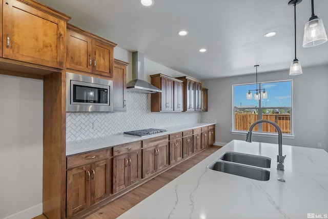 kitchen featuring sink, appliances with stainless steel finishes, light hardwood / wood-style flooring, backsplash, and wall chimney range hood