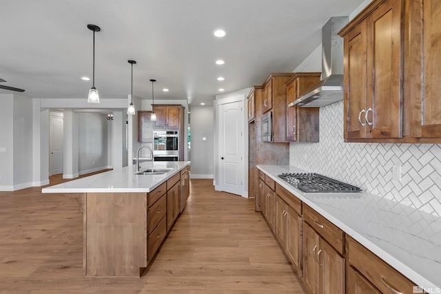 kitchen with hanging light fixtures, backsplash, light hardwood / wood-style floors, stainless steel appliances, and wall chimney range hood