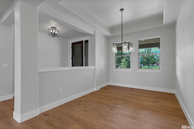 spare room with a raised ceiling, a chandelier, and light hardwood / wood-style flooring