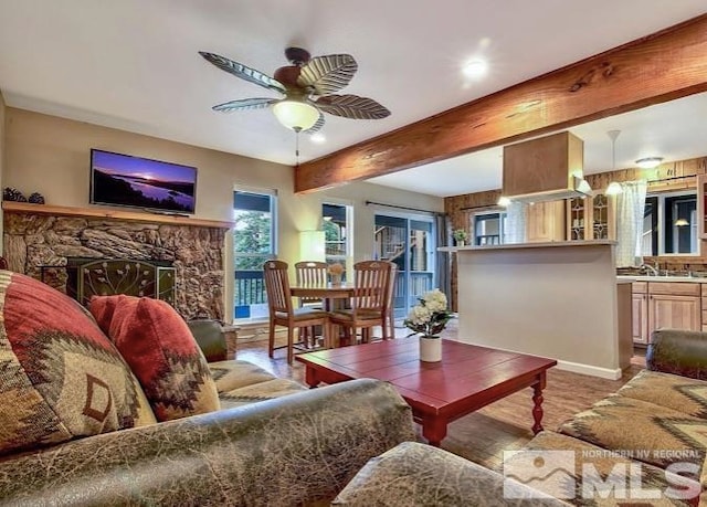 living room featuring ceiling fan, beam ceiling, a fireplace, and wood-type flooring