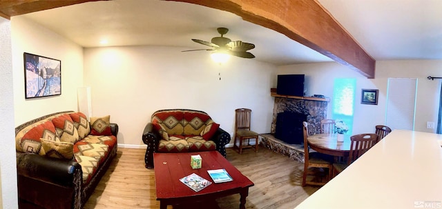 living room featuring ceiling fan, a stone fireplace, light hardwood / wood-style flooring, and beamed ceiling