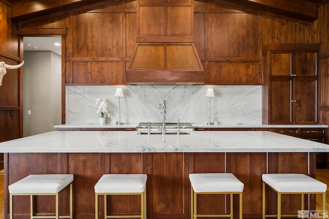 kitchen featuring sink, custom range hood, light stone counters, and a kitchen island