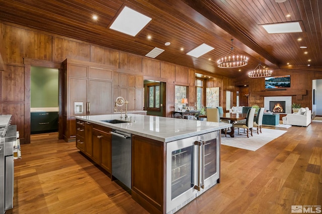 kitchen with beamed ceiling, wood walls, wood ceiling, light hardwood / wood-style flooring, and a kitchen island with sink