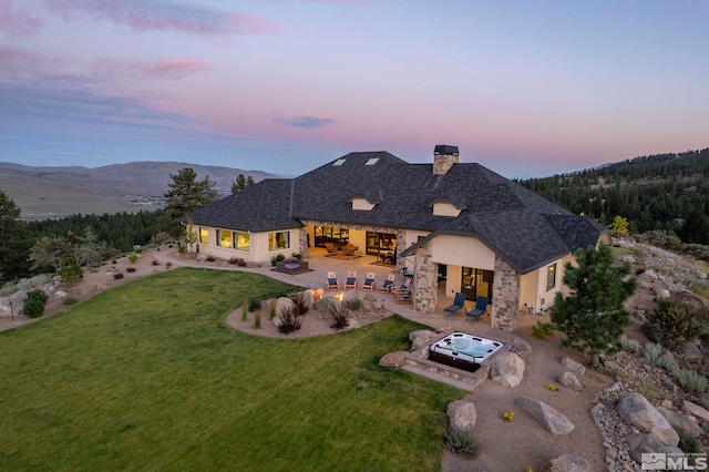 back house at dusk featuring a mountain view, a patio area, and a lawn