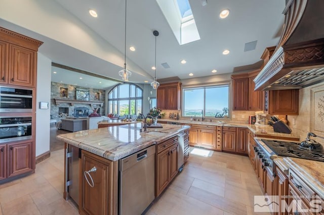 kitchen with decorative light fixtures, appliances with stainless steel finishes, light tile floors, light stone counters, and a kitchen island