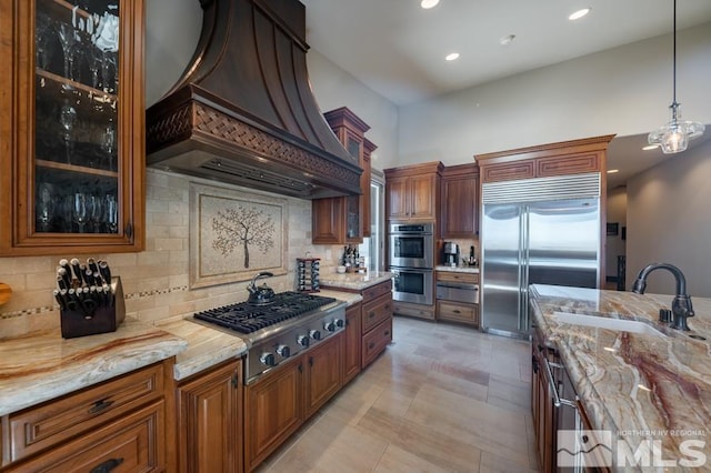 kitchen with appliances with stainless steel finishes, hanging light fixtures, custom range hood, tasteful backsplash, and light stone countertops