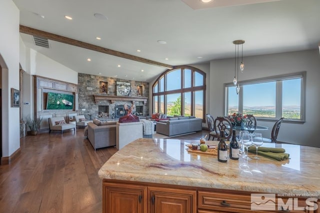 kitchen with dark hardwood / wood-style flooring, a wealth of natural light, light stone counters, lofted ceiling with beams, and a large fireplace