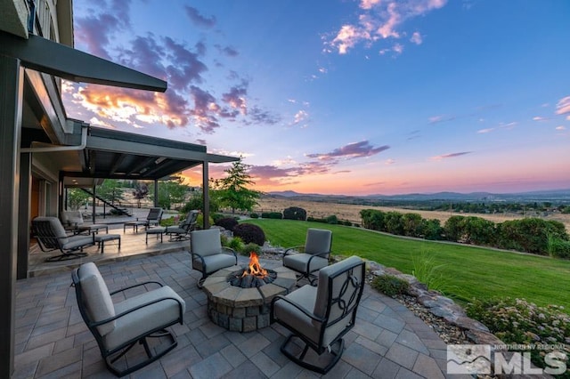 patio terrace at dusk with a lawn, an outdoor fire pit, and a rural view